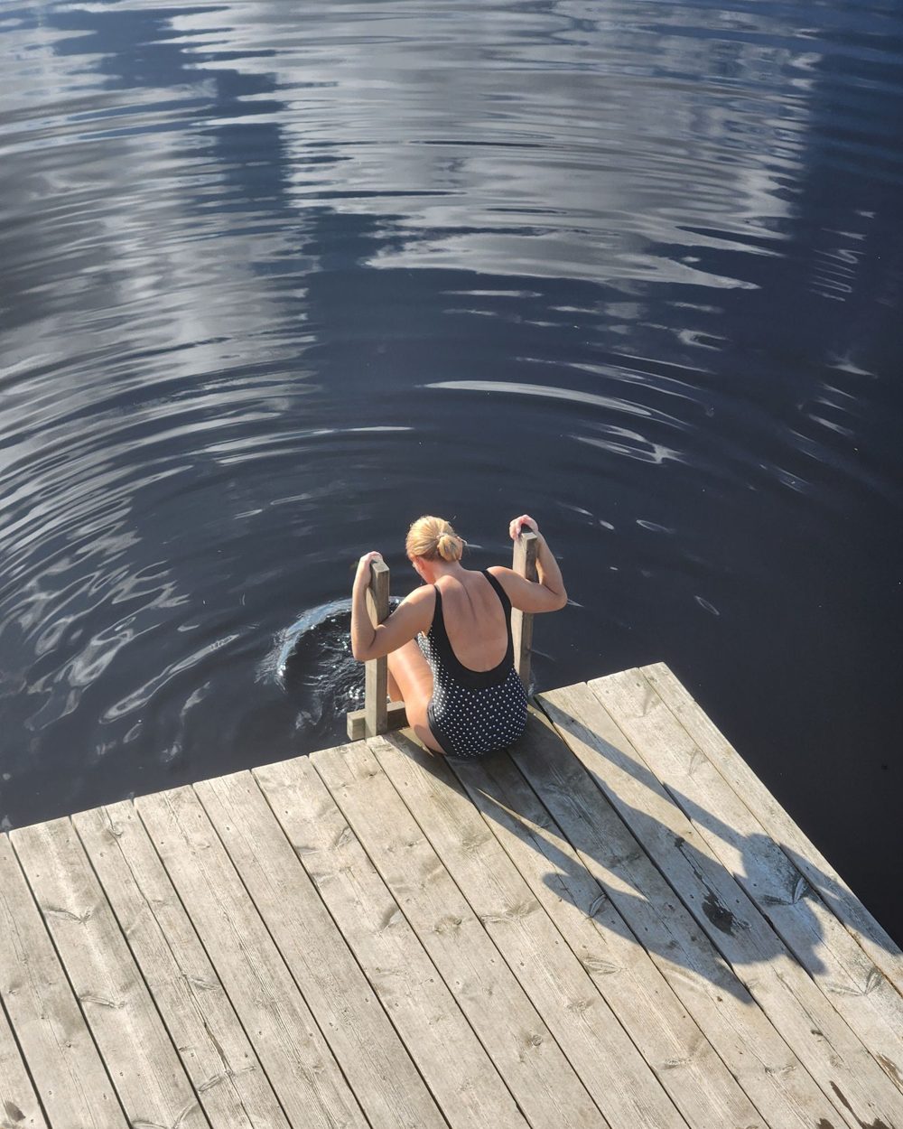 Nainen istuu uimalaiturilla järven rannalla